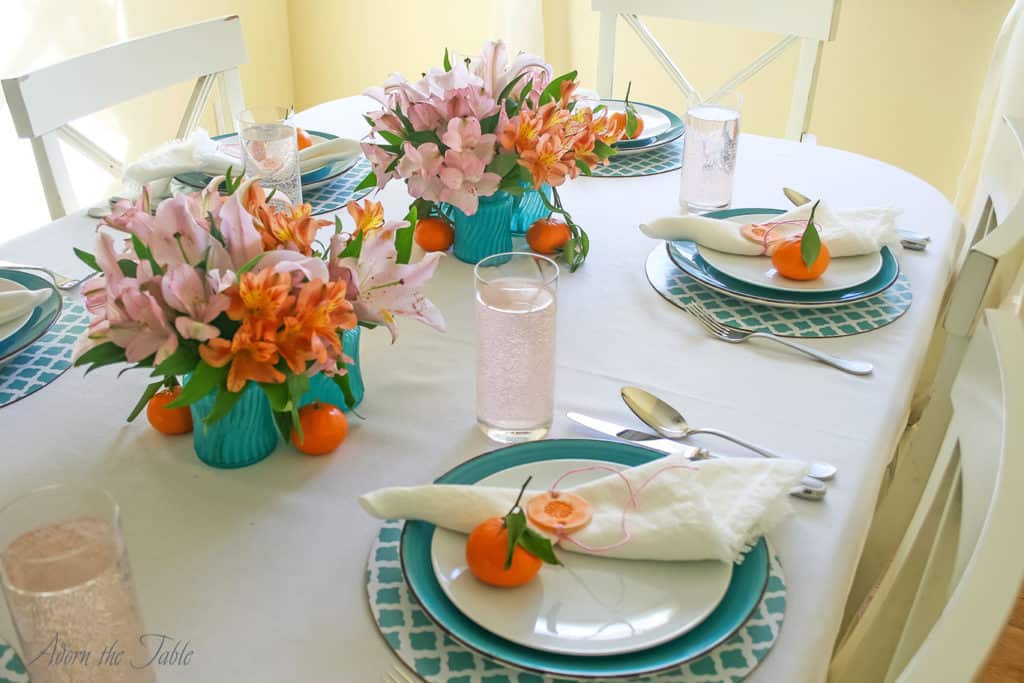 Centerpieces three ways - table setting side view of teal vases with teal plates and chargers. White napkins with orange napkin rings.