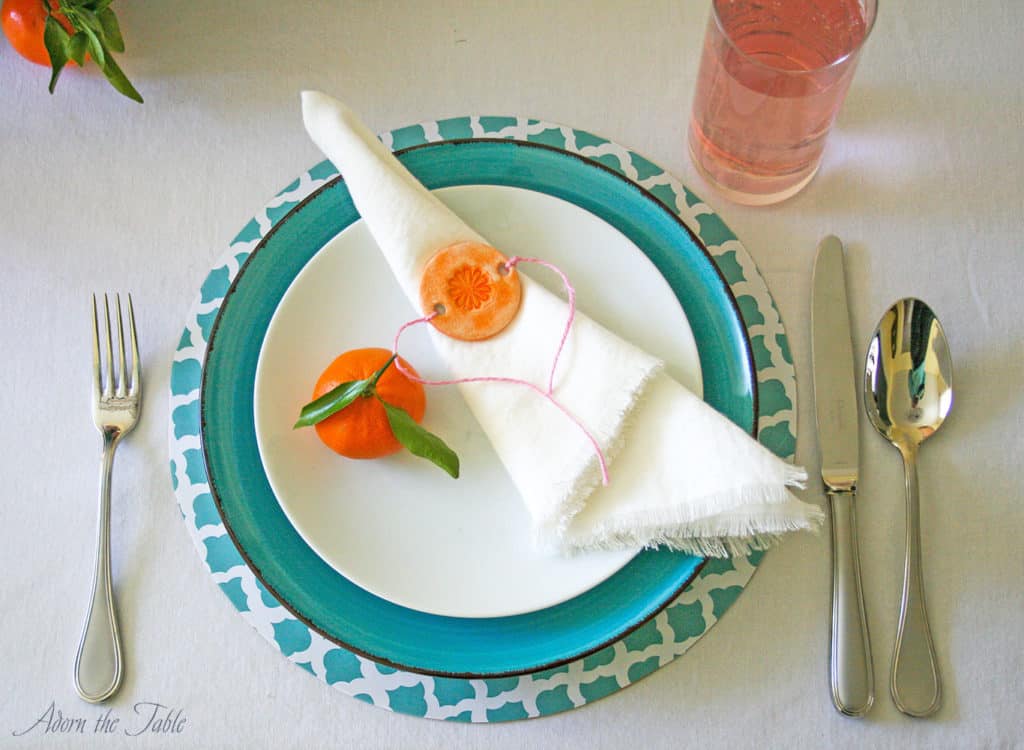 Mother's day place setting. Close up on teal and white diy charger, teal plate, white linen napkin and orange diy napkin ring.