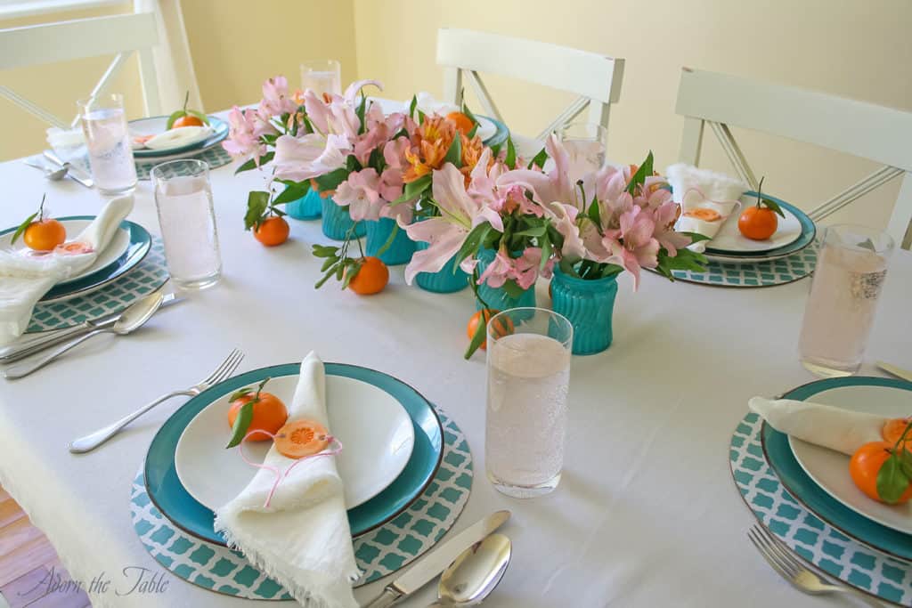 Centerpieces three ways - table setting angled view of 6 real vases in the middle of the table. With teal and white charger, teal plates and white linen napkins