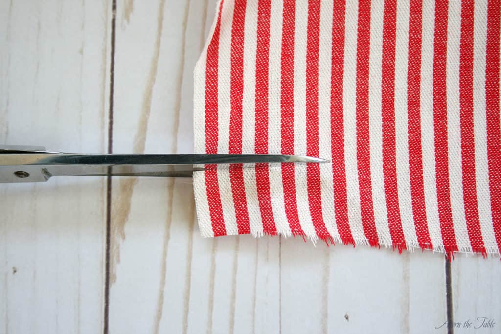 Scissors cutting red and white striped fabric