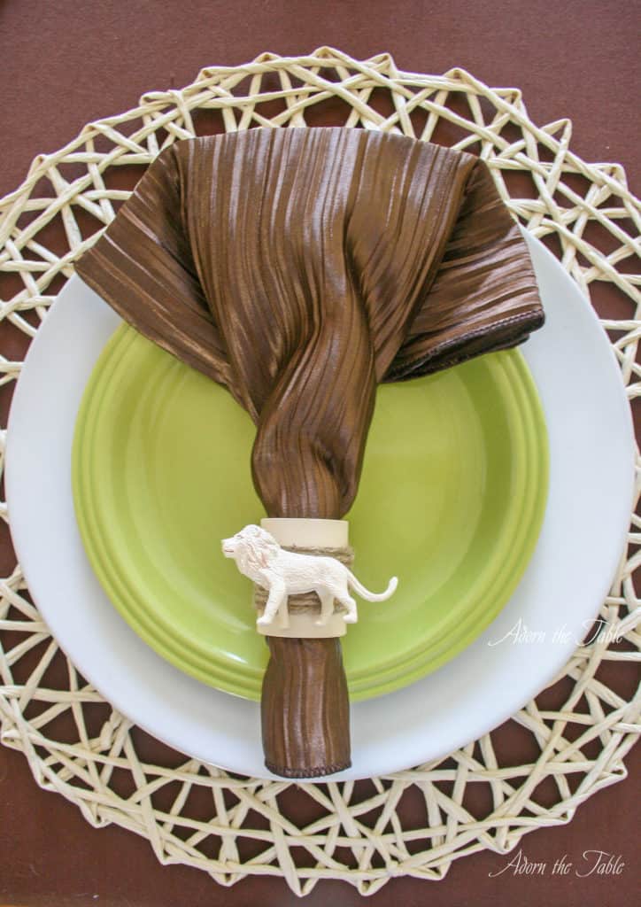 safari place setting with straw placemat, white plate, green plate, brown napkin and lion napkin ring