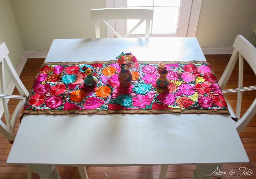 white kitchen table with multi-colored table runner and small vases on it