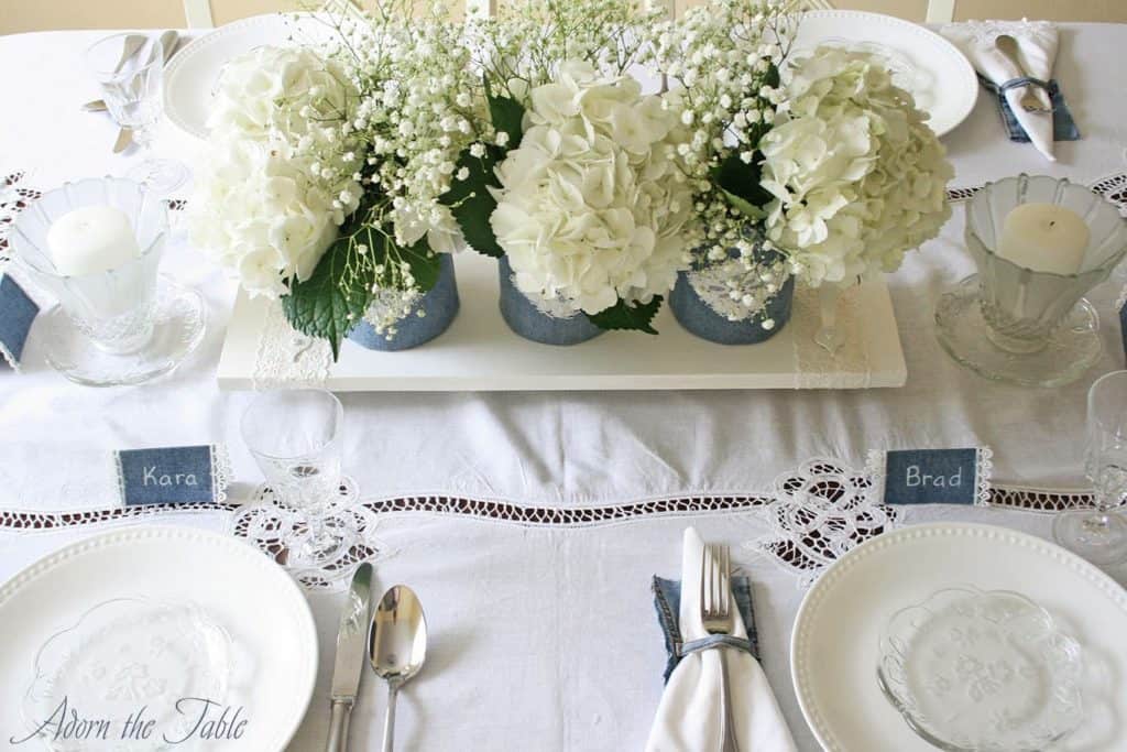 Overhead view of white lace tablecloth with denim and white place settings and denim covered vases.