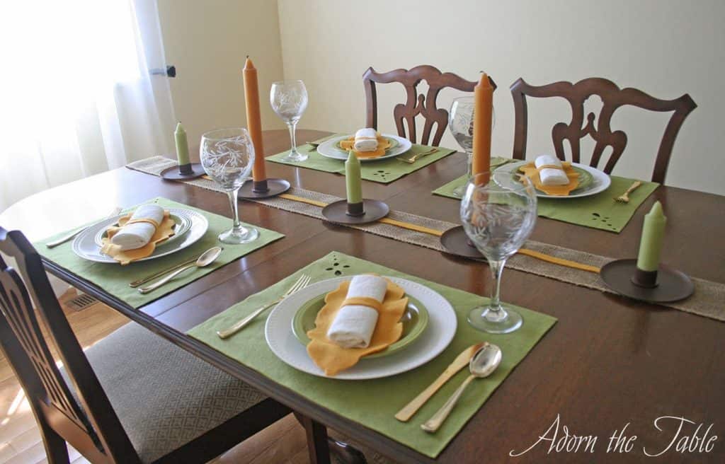 Fall table setting with green placemats, orange napkin ring and candles down the middle.