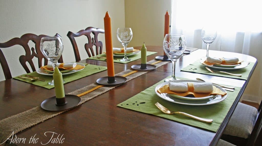 Fall table setting with green placemats, orange napkin ring and candles as the centerpiece.