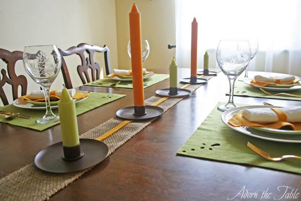 Fall table setting with row of green and orange candles as a centerpiece.