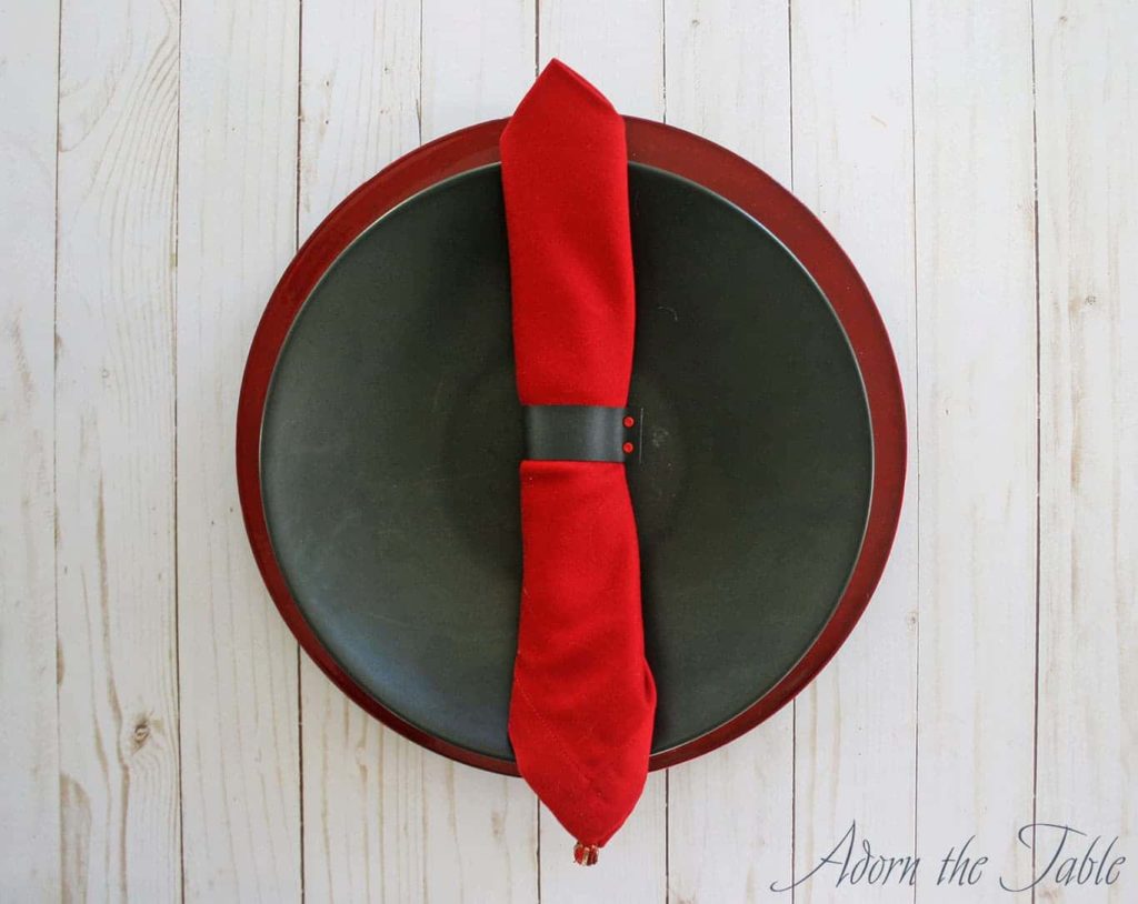 Diy faux napkin ring around red napkin. On black plate with red charger plate.