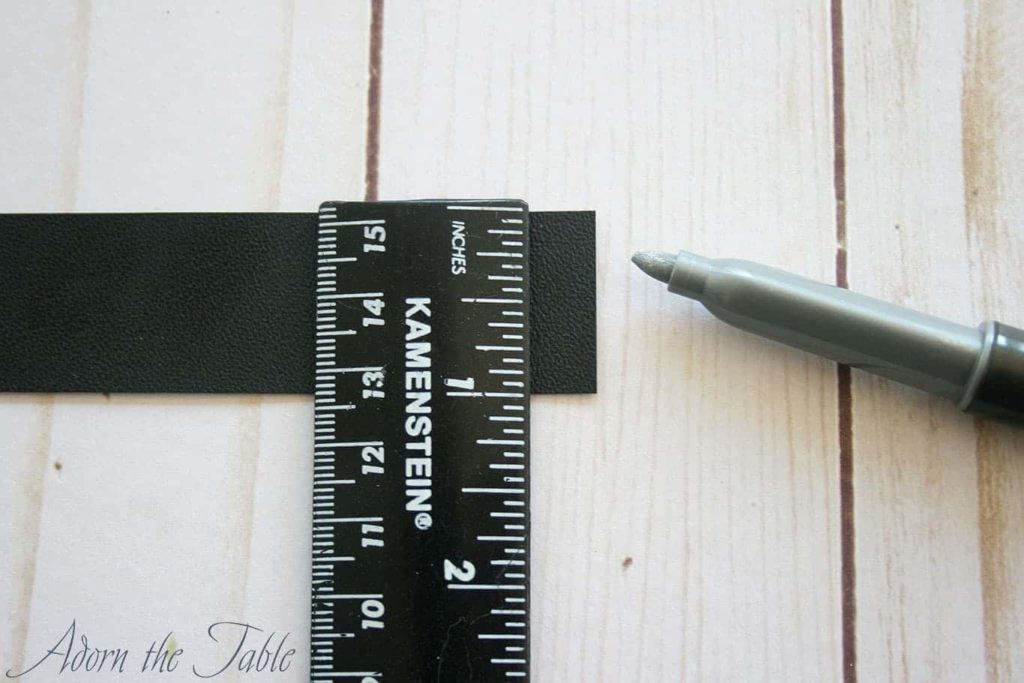 Ruler on black strip of faux leather with silver marker to the side.