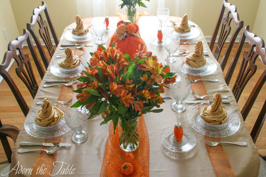 Pumpkin fall table setting for autumn. View from foot of the table. Orange flowers on orange mesh ribbon.