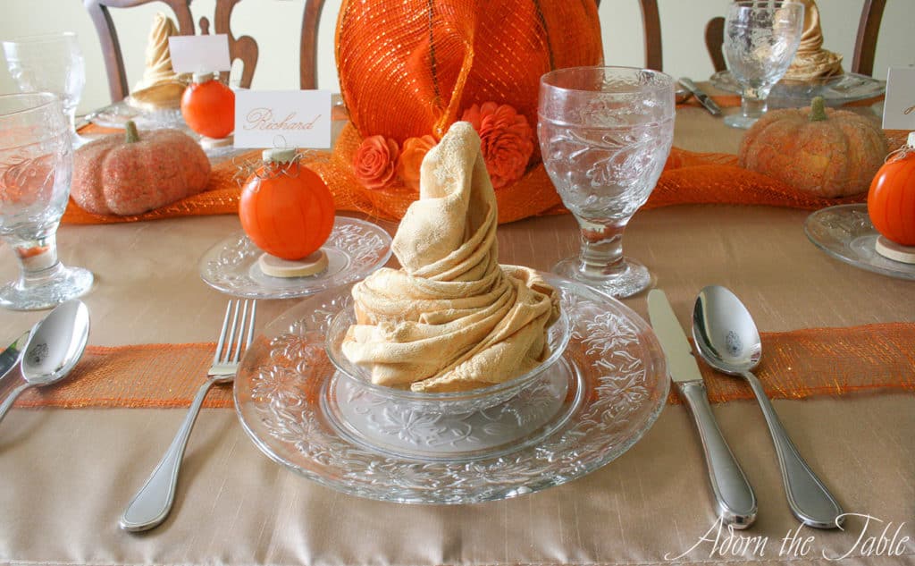 Autumn place setting with gold napkin on clear plates with a pumpkin place card holder. 