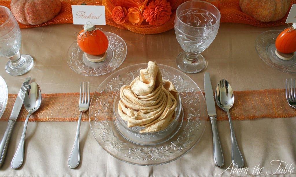 Fall place setting with gold napkin on clear plates with a pumpkin place card holder. 