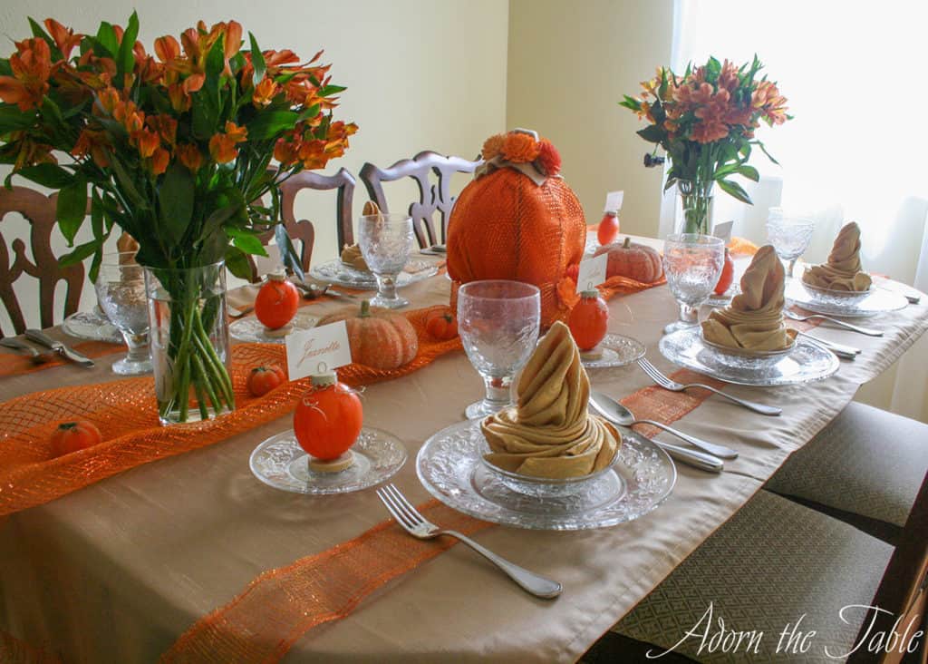 Right side view of pumpkin tablescape for Autumn. Orange flowers, diy pumpkin projects and clear plates for place settings. 