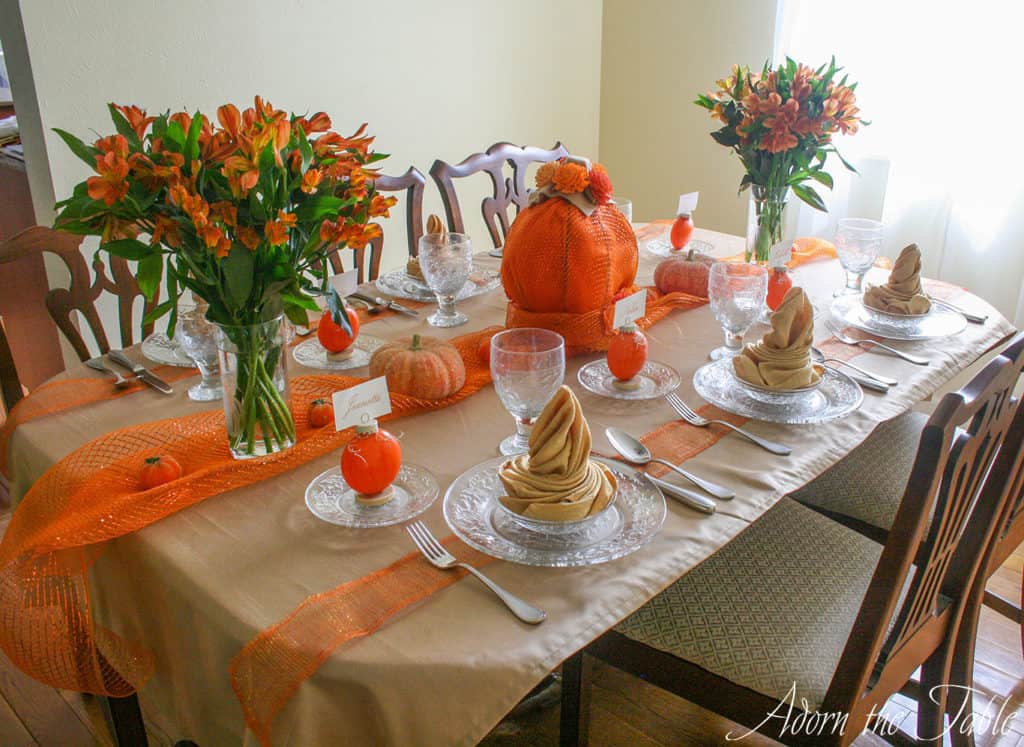 Left side of table setting for autumn using clear places, pumpkin place card holders, orange flowers and pumpkins