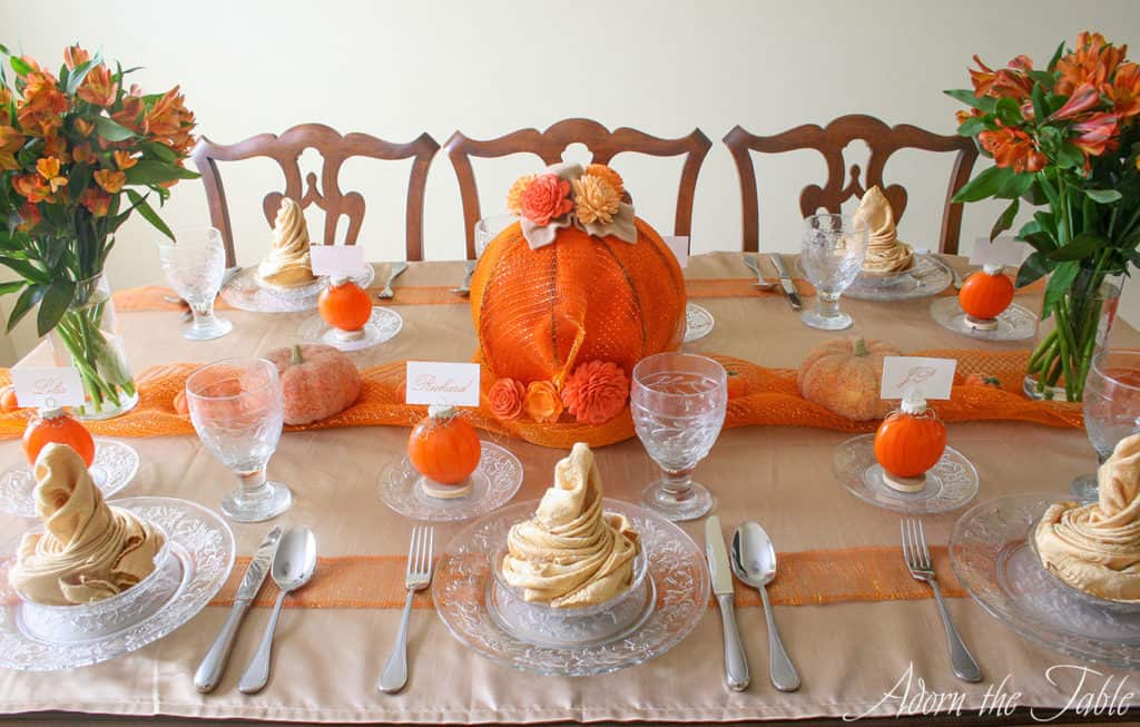 Side view of whole table setting for autumn with orange pumpkins and champagne napkins.