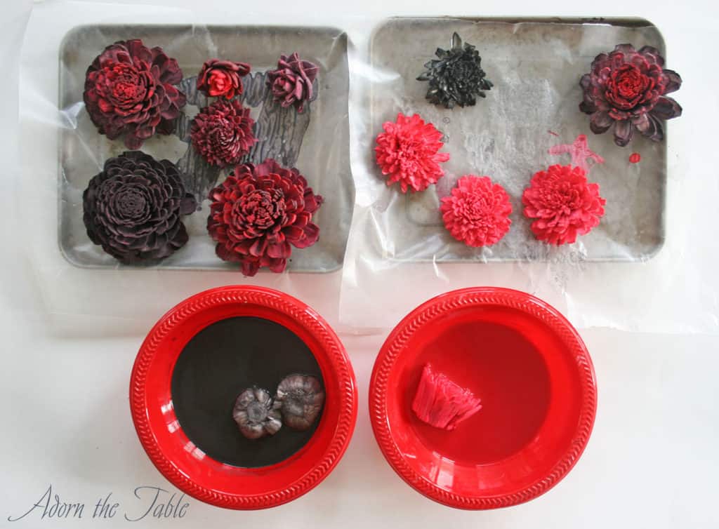 Sola wood flowers sitting in red and black paint baths with completed flowers drying on cookie sheets.