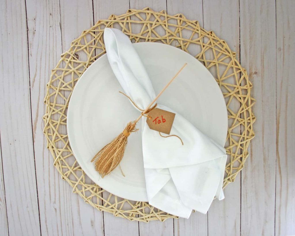 Witch's broomstick place card holder on white napkin and white plate.