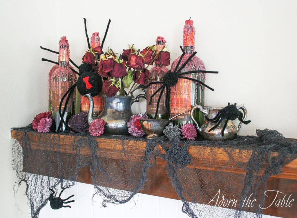 Creepy-Halloween-Mantel-Vignette with wax dripped wine bottles, fake black spiders and tarnished silver pieces. 