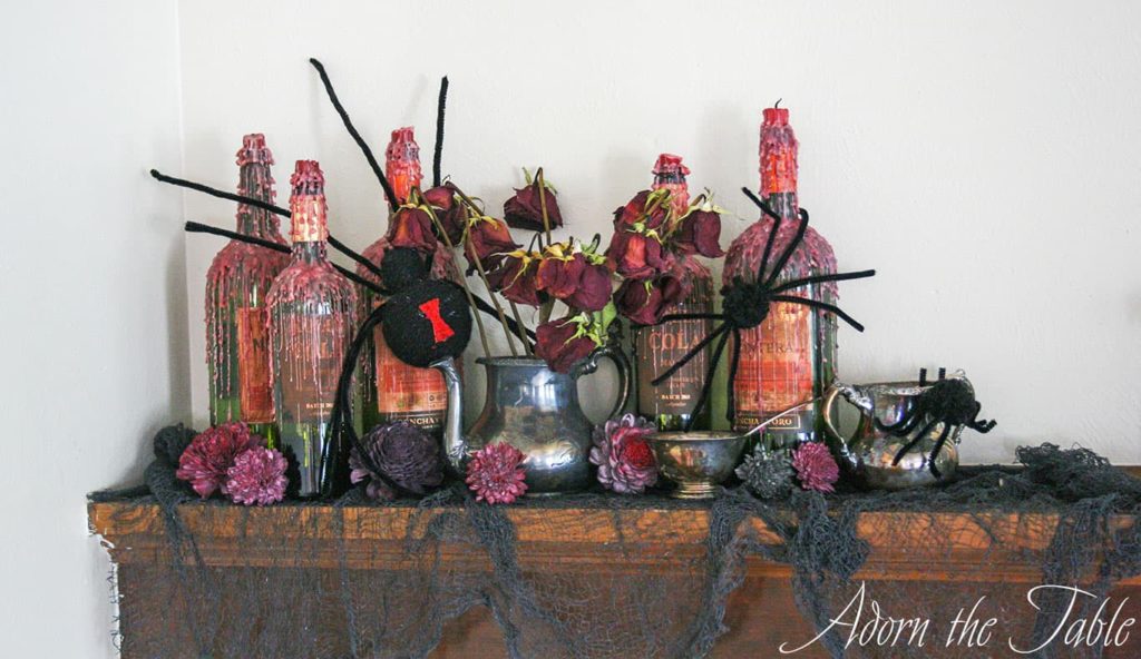 Creepy-Halloween-Mantel-Vignette with wax dripped wine bottles, fake black spiders and tarnished silver pieces. 