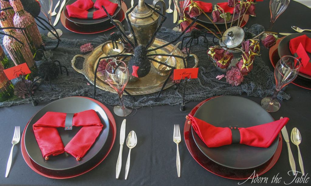 Creepy Halloween table setting with two place settings. Black plates on red chargers with red napkins.