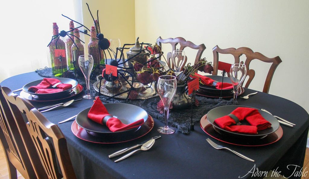 Creepy Halloween table setting. View from the cover showing black tablecloth, red and black place settings, spiders and tarnished silver.