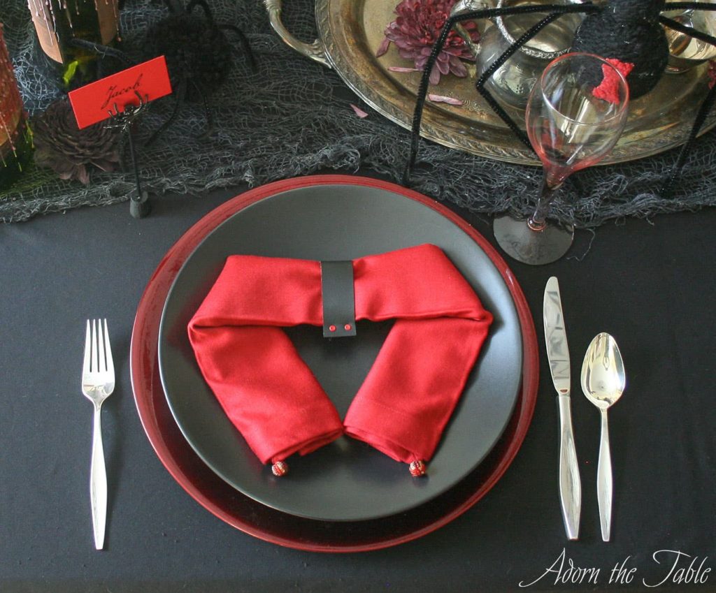 Creepy Halloween table setting with two place settings. Black plates on red chargers with red napkins folded like a spider.