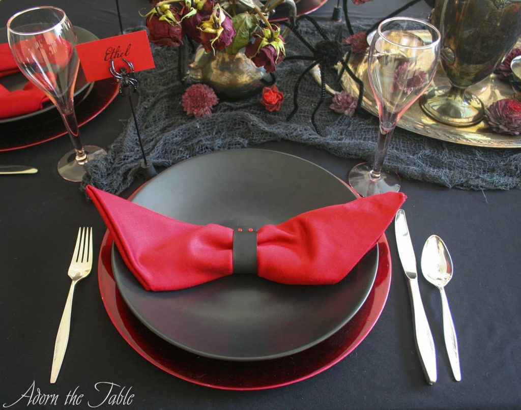 Creepy Halloween table setting with two place settings. Black plates on red chargers with red napkin folded like a bat