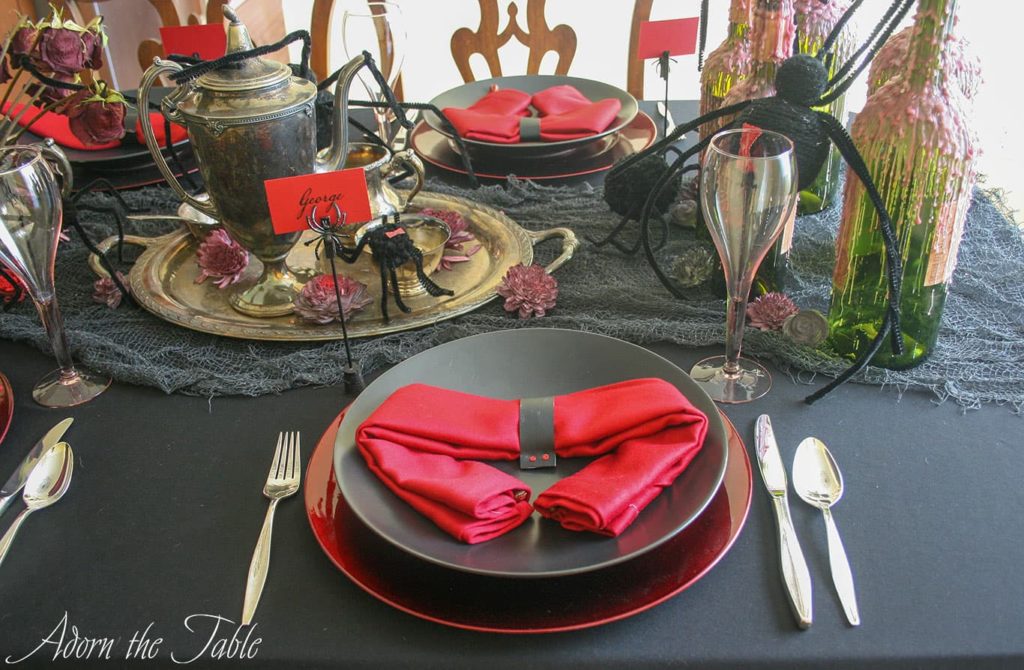 Creepy Halloween table setting with two place settings. Black plates on red chargers with red napkin folded like a spider