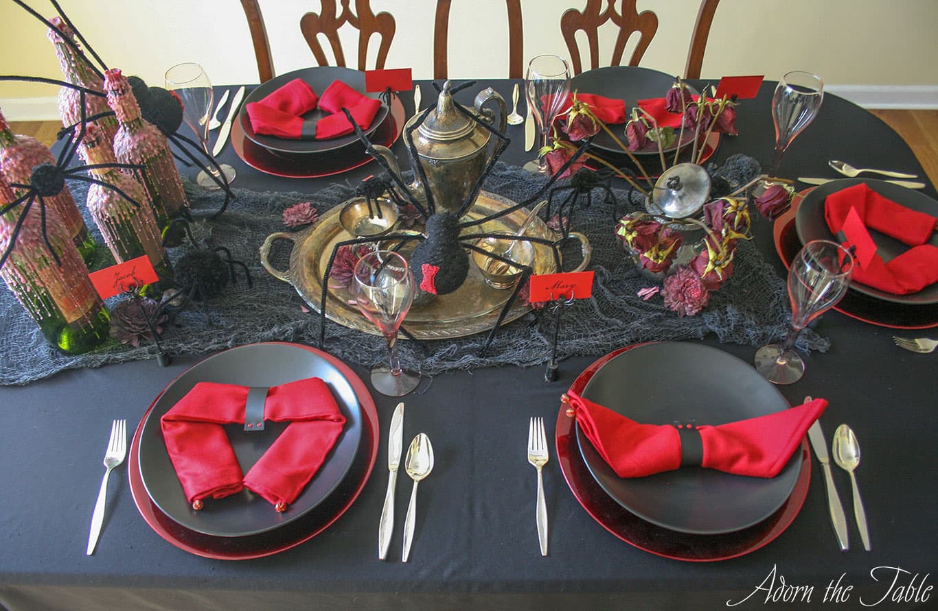 Side view of creepy Halloween table setting. Black tablecloth with red charges, black plates and red napkins