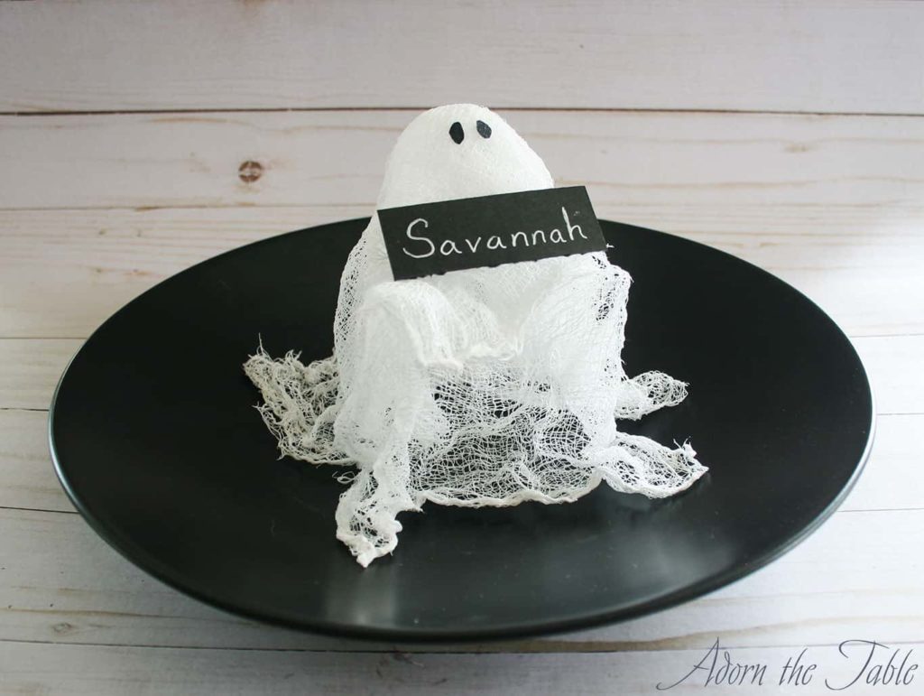 Halloween DIY Cheesecloth Ghost Place Card Holder with black eyes on a black plate holding a black name card