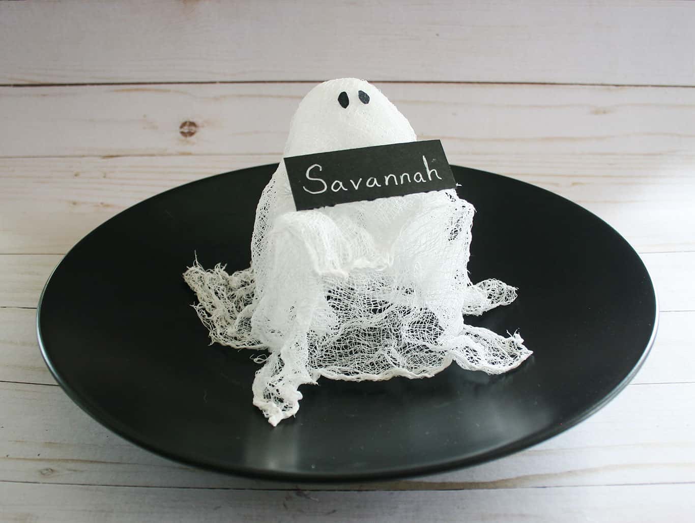 Cheesecloth Ghost DIY holding black name card on a black plate.