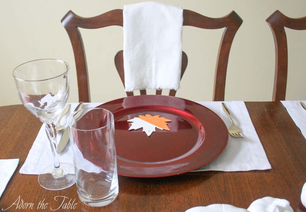White napkin hanging over chair with Thanksgiving day place setting on the table. 