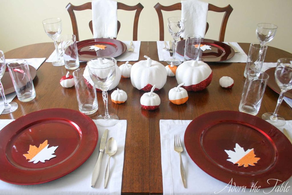 Thanksgiving Day place settings with white placemats, red chargers, and white napkins.