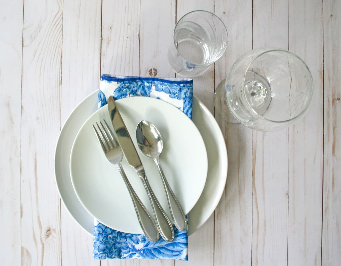 Ultimate list of must-have table setting pieces. White dishes with blue and white napkin, water glass and wine glass.