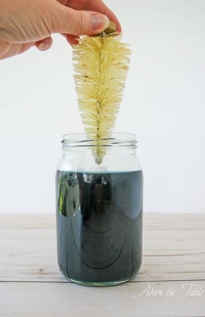 Placing natural colored bottle brush tree into jar with teal RIT dye bath.