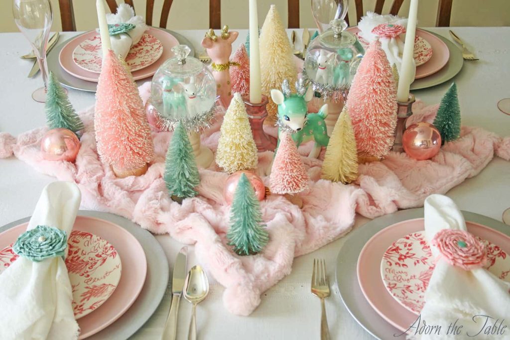 Pink and teal bottle brush trees on retro Christmas table with matching reindeer and place setting.