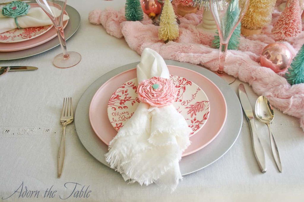 Place setting with silver charger, pink plate, red and cream salad plate and white napkin with pink napkin ring.
