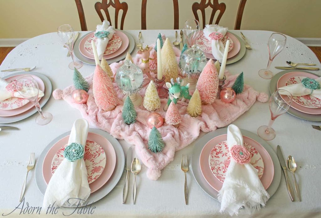 Pink and turquoise retro Christmas table setting on off-white tablecloth.