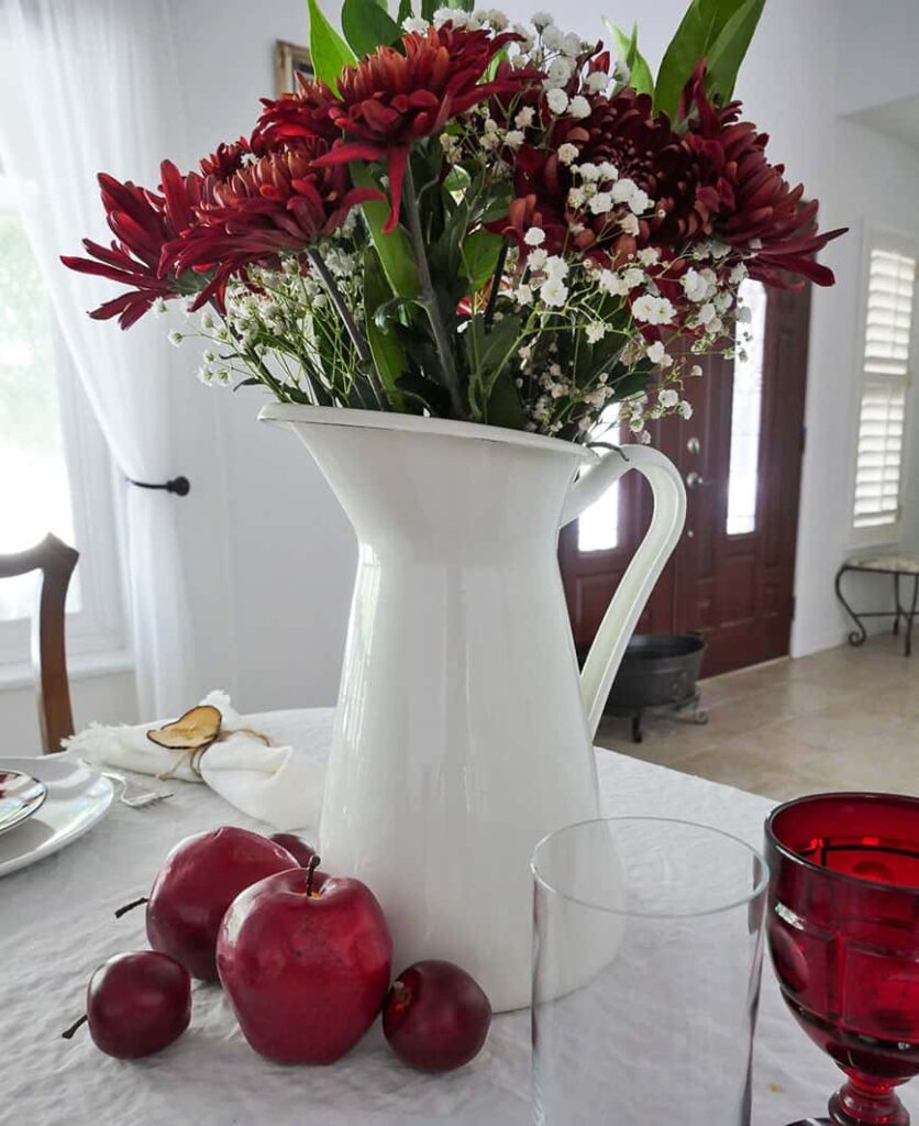 Close up of pitcher of flowers on table.