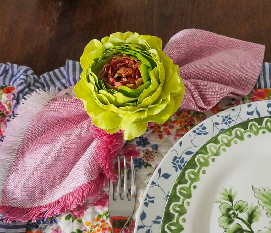 Raspberry colored napkin with large flower napkin ring around it.