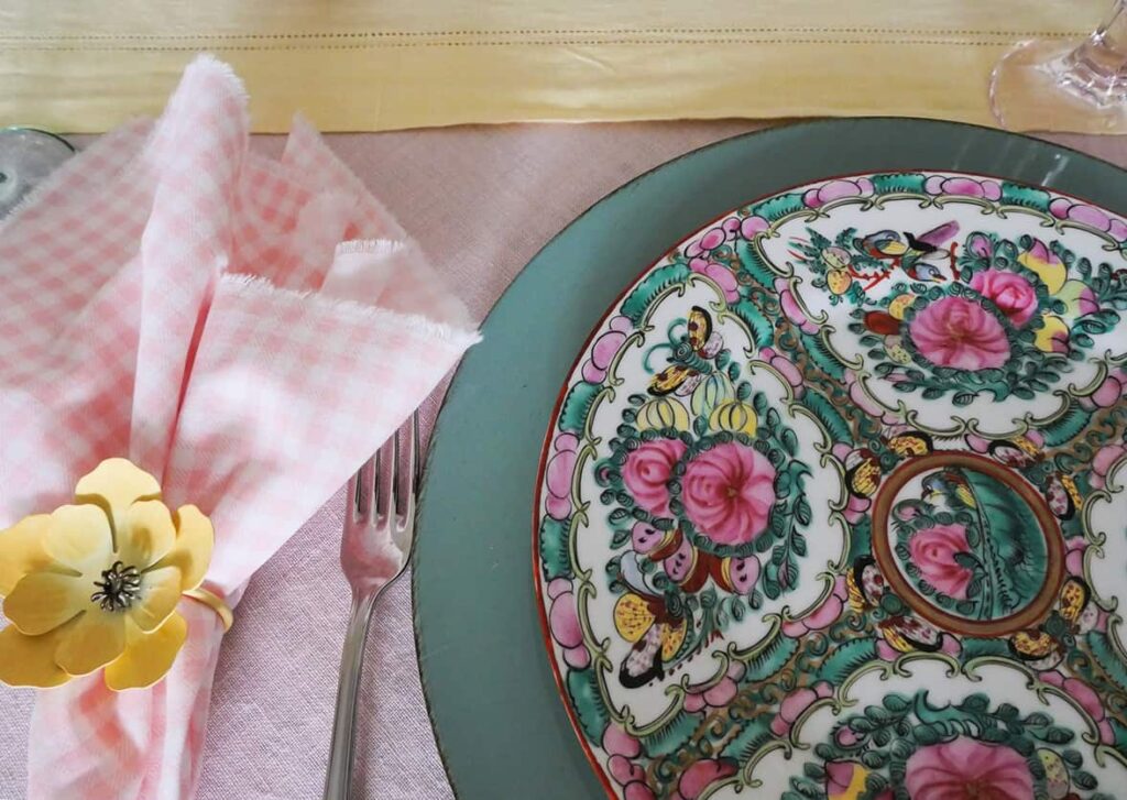 Teal charger plate under a multi-colored plate with a pick napkin on the left side.