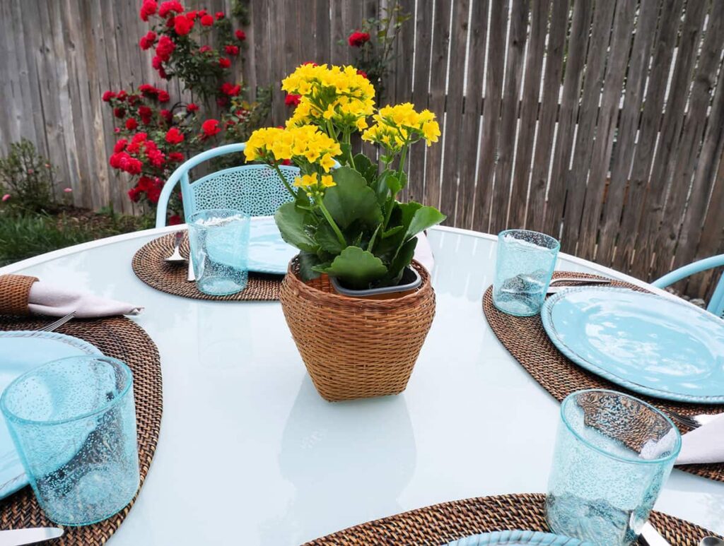 Outdoor thrifted table setting with simple centerpiece using a wicker basket and bright yellow flowers.