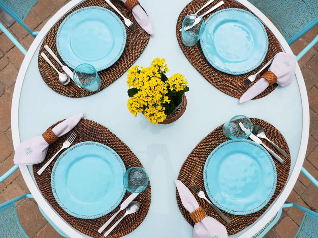 Overhead view of outdoor tablescape with rattan placemats and teal plates.