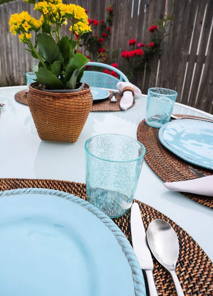 Al fresco tablescape with teal and medium rattan pieces.
