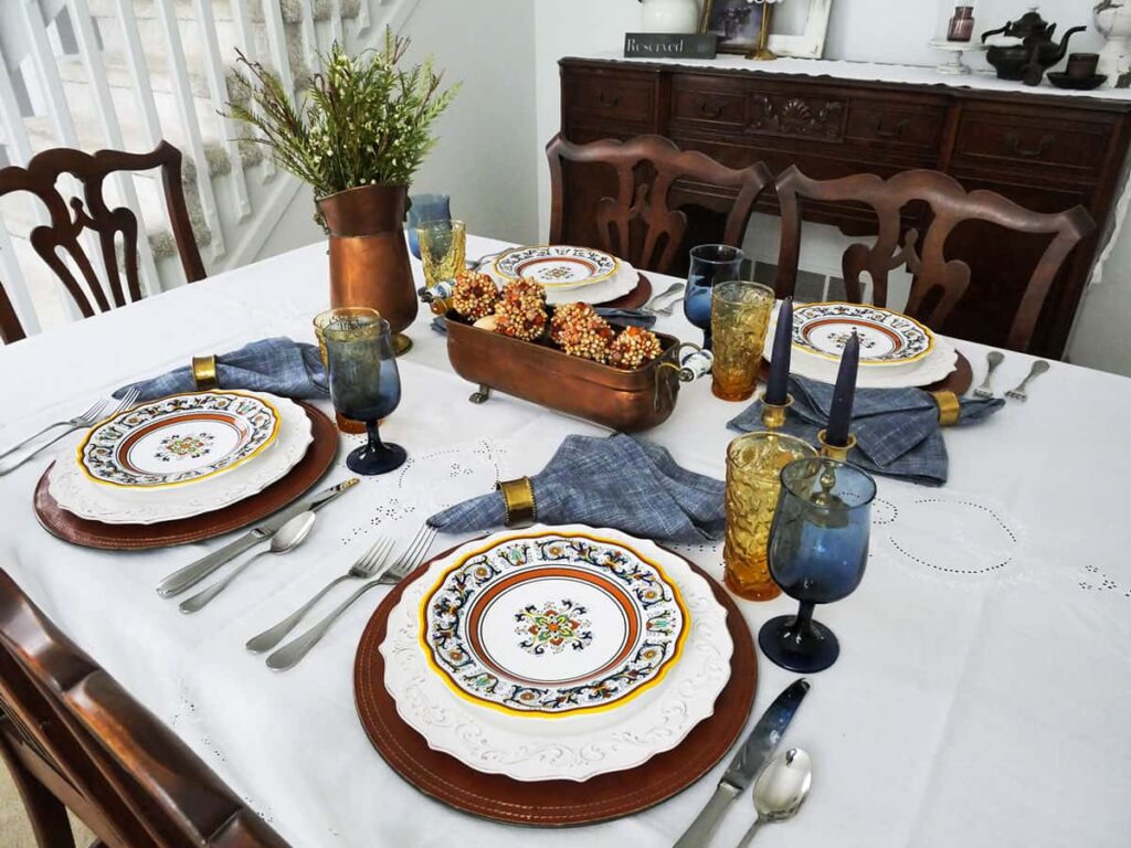 Fall table setting with a white tablecloth and copper accents.