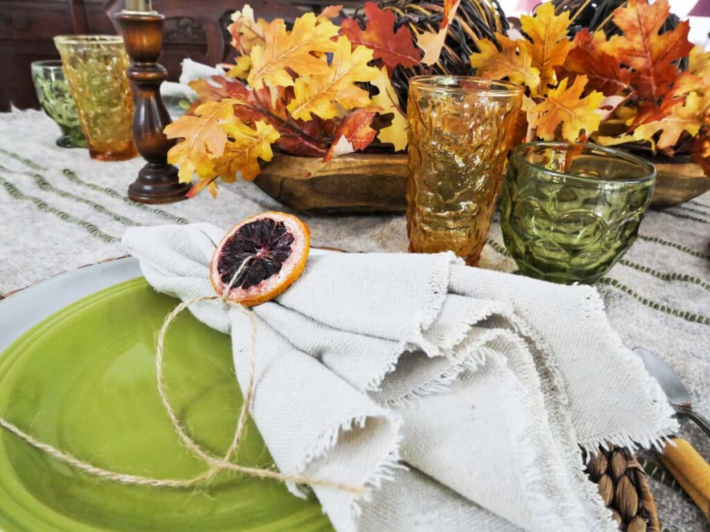 Cozy fall tablescape with dried orange slice on green plate.