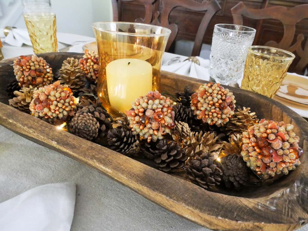 Shiny balls and pinecones inside a dough bowl on a fall tablescape.
