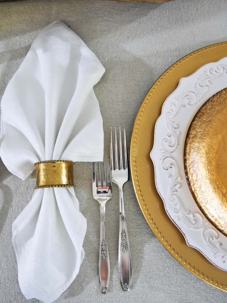 White napkin folded like a leaf with a gold napkin ring in the middle.