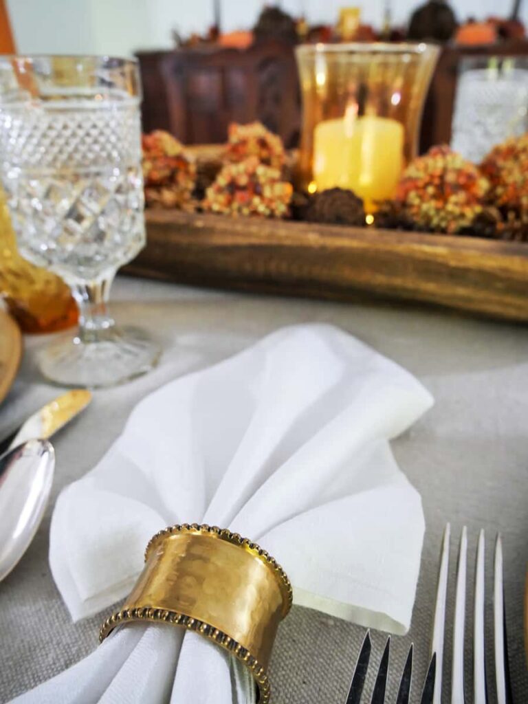 White napkin with gold napkin ring and rustic fall centerpiece in the background.